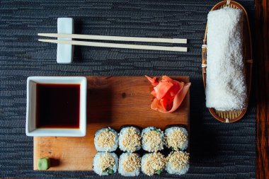 Masada soslu ve çubuklu bir tabak suşi. Suşi ahşap bir tepside ve tepside birkaç parça suşi var.