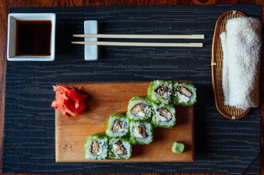 Çubuklu bir tabak suşi ve küçük bir kase sos. Suşi yeşil ve bir sürü malzemesi var.