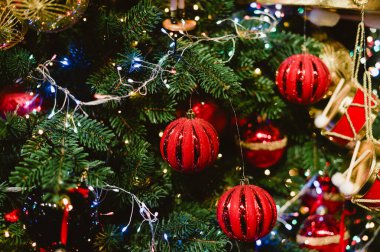 Kırmızı ve altın süslemeli bir Noel ağacı. Ağaç ışıklarla aydınlanıyor. Ağaçta üç kırmızı top var.