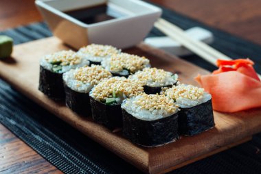 Bir tabak soslu suşi ve yemek çubuğu. Suşi ahşap bir tahtanın üzerinde düzgün bir sıra halinde düzenlenir.