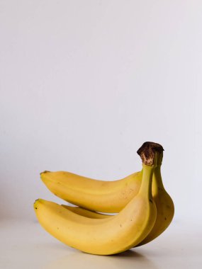 Beyaz bir masada üç muz oturuyor. Muzlar sarı ve olgun görünüyor. Tazelik ve bolluk kavramı, çünkü muzlar sağlıklı ve besleyici bir atıştırmalık seçeneği.