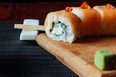 Üzerinde bir parça salatalık ve bir parça avokado olan bir suşi rulosu. Yuvarlak tahta bir kesme tahtasının üzerinde duruyor.