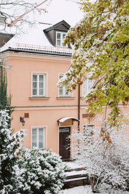 Karla kaplı çatısı olan bir ev. Ev kahverengidir ve beyaz süslemesi vardır.