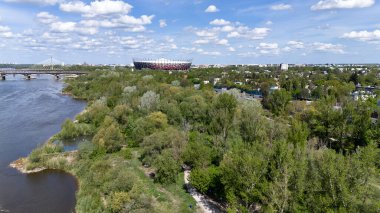 Köprüsü ve arka planında stadyum olan bir nehir. Gökyüzü mavi ve bulutlar var. Varşova 20.04.2025 Polonya ülkesi