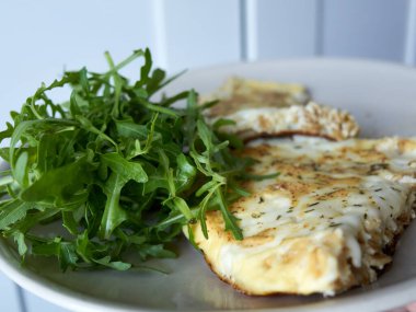 Bir tabak yemek, bir parça ıspanak ve bir parça peynir. Ispanak tabağın sol tarafında ve peynir de sağ tarafında.