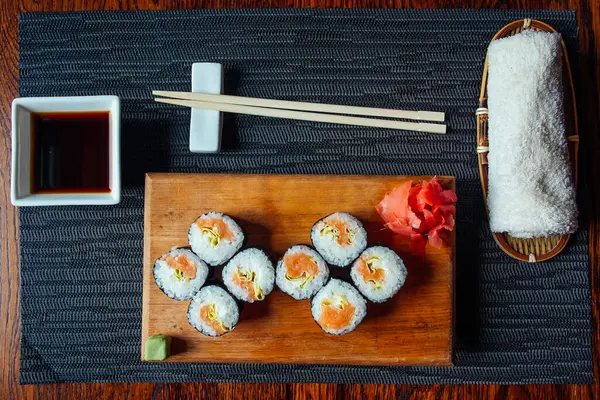 Çubuklu bir tabak suşi ve sos. Suşi ahşap bir tahtanın üzerinde düzgün bir sıra halinde düzenlenir.