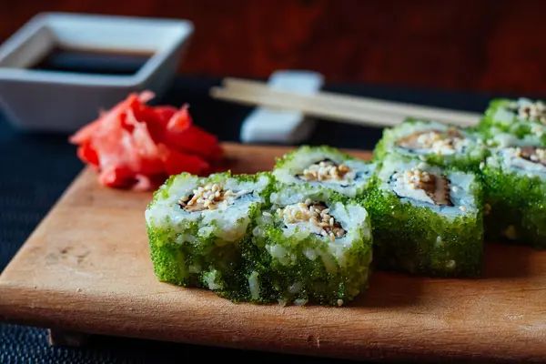 Yeşil yosun ambalajı ve kırmızı garnitürlü bir tabak suşi. Suşi ahşap bir masada oturuyor.