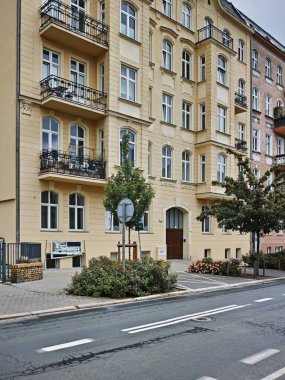 Önünde balkon ve ağaç olan büyük bir bina. Bina sarı ve bir sürü penceresi var. Poznan, Polonya 22.06.2024.