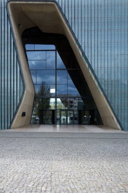 Binanın çok modern ve şık bir tasarımı var. Giriş, binaya açıklık ve şeffaflık hissi veren büyük cam bir pencereden oluşuyor. Bina bir şehirde yer almaktadır. Varşova 15.04.2025, Polonya