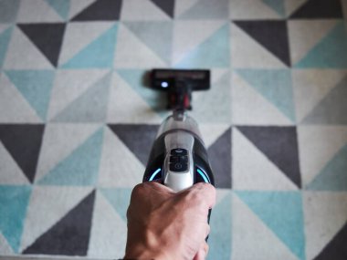 Biri elinde mavi ve gri desenli bir elektrikli süpürge tutuyor. Elektrik süpürgesinin üzerinde mavi bir ışık var.