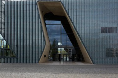 Binanın çok modern ve şık bir tasarımı var. Giriş, binaya açıklık ve şeffaflık hissi veren büyük cam bir pencereden oluşuyor. Bina bir şehirde yer almaktadır. Varşova 15.04.2025, Polonya