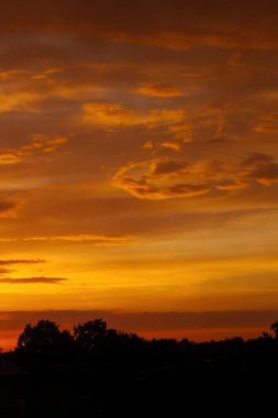 Gökyüzü turuncu ve bulutlar beyaz. Güneş batıyor ve gökyüzü bulutlarla dolu. Telefon duvar kâğıdı. Dikey arkaplan.