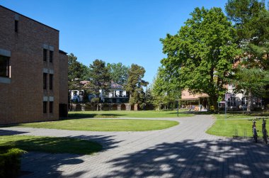 Önünde avlu olan tuğla bir bina. Avluda bir patika ve bank var.