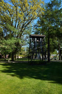 Tepesinde çan olan uzun kule çimenli bir tarlada duruyor. Kule ağaçlarla çevrili ve o bir parkın parçası. Varşova, Polonya 01-05-2025. Kutsal Bakire Meryem 'in Doğuşu Kilisesi.