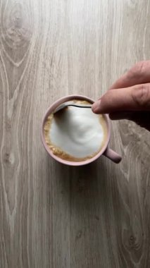 Bir fincan kahve ahşap bir masada oturur. Kahve sıcak ve üzerinde kremalı bir köpük var. Sıcaklık ve rahatlık kavramı, kahve rahatlama ve keyif için popüler bir içecektir.