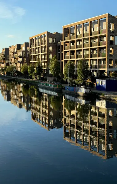 Brentford, Batı Londra 'daki modern kanal kenarı daireleri, iki dar tekne ile birlikte ağaçlık yamaçlara demirlemiş olarak suya yansıdı. Mavi gökyüzü ile güneşli güzel bir gün..