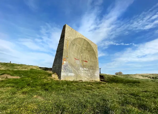 Güneşli bir günde İngiltere, Kent 'teki Abbot' s Cliff 'te beton bir ses aynası. İnşaat, denize bakan çimenli bir uçurumun kenarında duruyor. Bulutlar ve mavi bir gökyüzü arkasında.