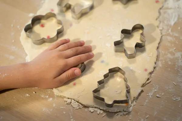 child participates in preparation of homemade gingerbread cookies. Closeup of a childs hand cutting out cookies using cookie cutters on cutting board. Delicious sweet homemade cake.