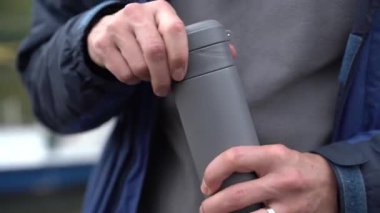 Adamın biri termos bardağını sıcak bir içecekle açıyor. Çevre dostu kahve fincanı..