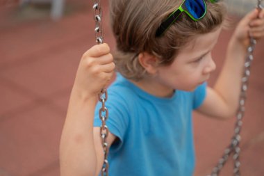 Mavi tişörtlü küçük çocuk boş parkta neşeyle sallanıyor. Küçük çocukların gerçek açık hava yaşam tarzı. Fotoğrafı kapat..