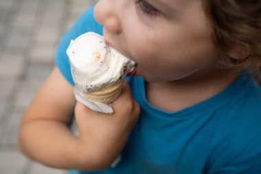 Mavi tişörtlü, vanilyalı dondurmayı çikolata parçacıklarıyla yalayan çocuğun yakın çekimi. Mükemmel yaz ferahlatıcı anı.