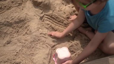 Mavi tişörtlü ve güneş gözlüklü şirin bir çocuk oyun parkındaki kumdan yapılmış. Çocukluk, açık hava aktiviteleri ya da yaz tatili eğlencesi gibi konular için ideal.