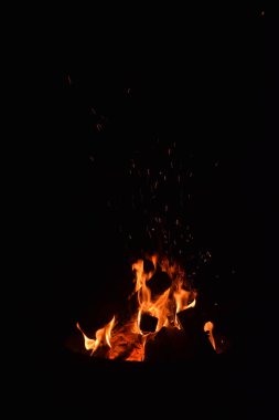 Karanlık bir gece gökyüzüne karşı parlayan şenlik ateşinin büyüleyici bir görüntüsü. Alevler dans eder ve titreşir. Ahşap kütükler çaprazlar, ateş tarafından tüketilirken benzersiz bir şablon oluşturur.. 