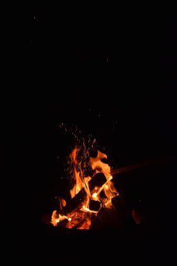 Karanlık bir gece gökyüzüne karşı parlayan şenlik ateşinin büyüleyici bir görüntüsü. Alevler dans eder ve titreşir. Ahşap kütükler çaprazlar, ateş tarafından tüketilirken benzersiz bir şablon oluşturur.. 