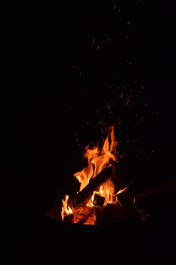 Karanlık bir gece gökyüzüne karşı parlayan şenlik ateşinin büyüleyici bir görüntüsü. Alevler dans eder ve titreşir. Ahşap kütükler çaprazlar, ateş tarafından tüketilirken benzersiz bir şablon oluşturur.. 