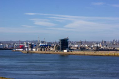 Arkaplanda geniş şehir manzarasının yer aldığı canlı bir sahil manzarası. Bir dalgakıran denize doğru yayılır ve şehir ile açık deniz arasında doğal bir bariyer oluşturur.. 