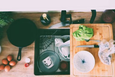 Mutfak dağınıklığı. Kirli bulaşıklarla dolu bir mutfak lavabosunun tepeden tırnağa görüntüsü. Bir tava, bir bıçak, bir kesme tahtası, yumurtalar ve lavaboda çeşitli tabak ve kaseler var.. 