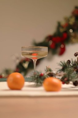 Festive Fizz. Köpüklü bir içecek, mandalina ve çam kozalakları ve arka planda kırmızı böğürtlenlerle süslenmiş kırmızı bir çelenk dolu şenlik masası.