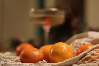  Köpüklü bir içecek dolu bir coupe kaburga bardağıyla şenlik masası. Ağ torbada mandalinalar ve arka planda çam kozalakları ve kırmızı böğürtlenlerle süslenmiş çam çelengi.