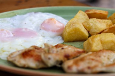 Kızarmış patates, tavuk fileto, mavi tabakta iki kızarmış yumurta bıçaklı, ahşap yüzeyde çatal. Yüksek kalite fotoğraf