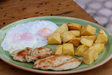 Kızarmış patates, tavuk fileto, mavi tabakta iki kızarmış yumurta bıçaklı, ahşap yüzeyde çatal. Yüksek kalite fotoğraf