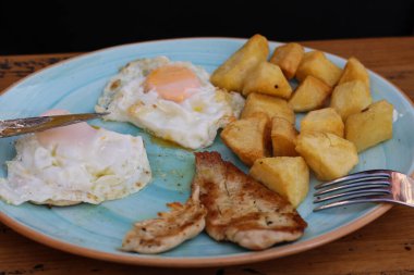 Kızarmış patates, tavuk fileto, mavi tabakta iki kızarmış yumurta bıçaklı, ahşap yüzeyde çatal. Yüksek kalite fotoğraf