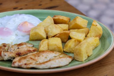 Kızarmış patates, tavuk fileto, mavi tabakta iki kızarmış yumurta bıçaklı, ahşap yüzeyde çatal. Yüksek kalite fotoğraf
