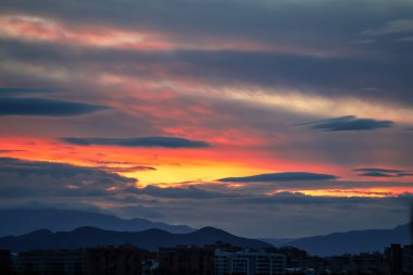 Malaga, İspanya üzerinde mavi saat manzarası, parçalı bulutlu sarı ve kırmızı gökyüzü - arka planda bulutlu dağlar. Yüksek kalite fotoğraf
