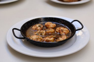 Gambas Pil İspanyol yemeği geleneksel dökme demir tavada servis ediliyor, masa üstü beyaz tabakta. Yanında ekmekle servis ediliyor. Yüksek kalite fotoğraf.