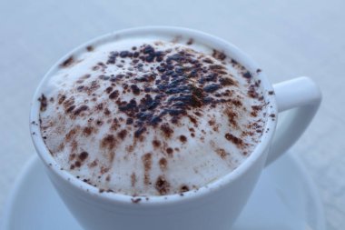 Beyaz fincanda çikolata ve beyaz yüzeyde çay tabağı ile kapuçino serpiştirilmiş bir fincan kahve. Yüksek kalite fotoğraf