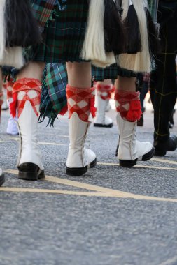Düşük açılı bir görüntü, Silahlı Kuvvetler Günü Geçit Töreni sırasında geleneksel İskoç etekleri ve tartan çoraplarıyla katılımcıların bacaklarını yakalıyor. Görüntü, arka perspektiften senkronize hareketi vurgular.
