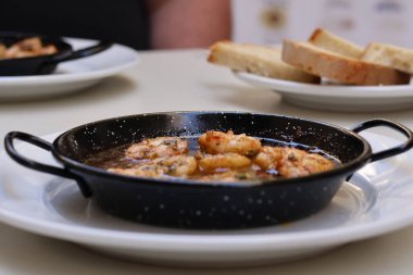 Gambas Pil İspanyol yemeği geleneksel dökme demir tavada servis ediliyor, masa üstü beyaz tabakta. Yanında ekmekle servis ediliyor. Yüksek kalite fotoğraf.