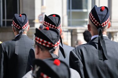 İskoçya 'nın Aberdeen kentinde düzenlenen Silahlı Kuvvetler Günü Geçit Töreni sırasında üniformalı gaziler kol geziyor. Arka plan, halkın kutlamalarının bir parçası olan disiplinli hareketlerini ve törensel başlıklarını vurguluyor.