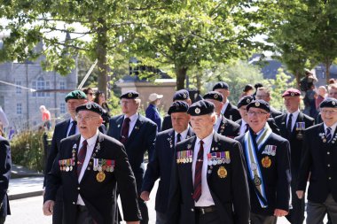 İskoçya 'nın Aberdeen kentinde düzenlenen Silahlı Kuvvetler Günü Geçit Töreni sırasında üniformalı gaziler kol geziyor. Arka plan, halkın kutlamalarının bir parçası olan disiplinli hareketlerini ve törensel başlıklarını vurguluyor.