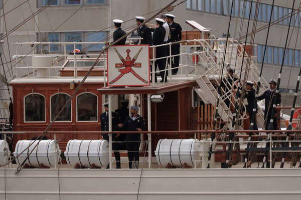 Высокий Корабль покидает Порт Абердин. На палубе стоит экипаж Оманского Высокого Корабля, который машет зрителям на Фестивале Высоких Кораблей в Абердине. Их присутствие придает яркую атмосферу и демонстрирует международное товарищество мероприятия.