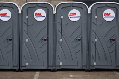 Kapıda CAP Etkinlik Hizmetleri logosu bulunan, beyaz kapaklı, özdeş, portatif tuvaletlerin göz hizasında çekimleri.