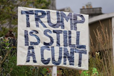 Aberdeen 'deki bir gösteri sırasında yeşil yapraklar arasında yaşayan kişilerin güçlü Trump karşıtı tutumlarını gösteren bir protesto tabelasının yakın çekimi. Bu işaretler merkezi. Trump ziyareti sırasında kamuoyunun yoğun görüşünü yansıtıyor.. 