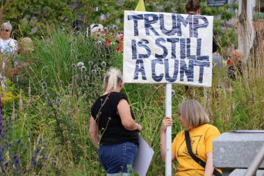 Aberdeen 'deki bir gösteri sırasında yeşil yapraklar arasında yaşayan kişilerin güçlü Trump karşıtı tutumlarını gösteren bir protesto tabelasının yakın çekimi. Bu işaretler merkezi. Trump ziyareti sırasında kamuoyunun yoğun görüşünü yansıtıyor.. 