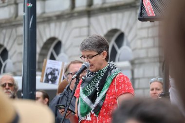 Konuşmacı, Aberdeen 'deki bir protestoda mikrofona tutkuyla konuşuyor. Arkaplanda bulanık figürler ve şehir mimarisi ile mesajının ciddiyetini aktarıyor.