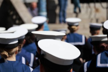 Arkadan yakından bakınca, koyu mavi üniformalı, düz şapkalı, lacivert üniformalı birçok kişi görülüyor. Görünür yüzleri veya özel işaretleri olmayan başları ve omuzlarına verilen ilgi, birlik ve disiplini vurguluyor..